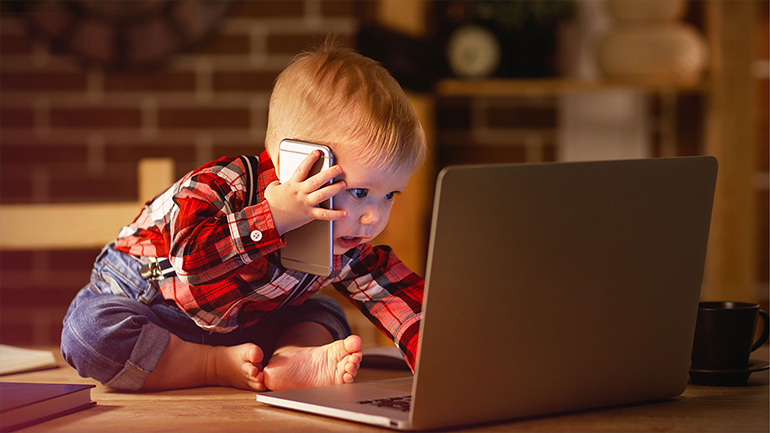 A képen egy gyermek látható a számítógép előtt aki éppen a képernyőhöz nyúl.